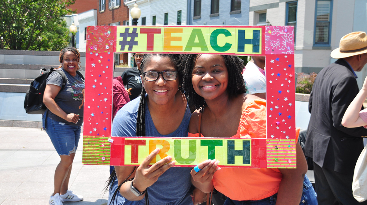 Two women posing in a frame that reads "#TEACH TRUTH"