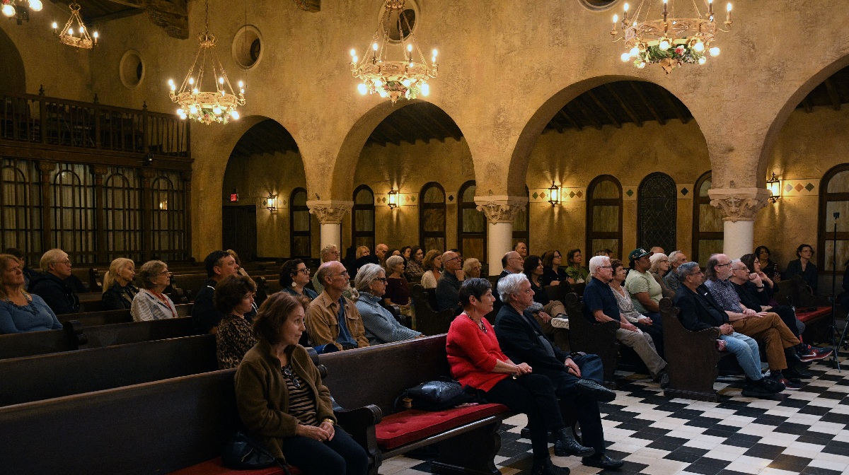 Photo of fifty people seated in pews, facing the front of a church.